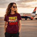 Woman wearing a 'TRUJET' t-shirt with an airplane graphic, standing on an airport tarmac with an airplane in the background.