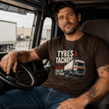 Male lorry driver wearing dark brown Tyres and Tachos HGV graphic t-shirt sitting in the cab of an artic lorry at a transport depot