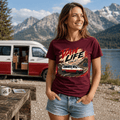 Woman wearing a 'Van Life Live It' t-shirt with a van and nature graphic, standing in front of a scenic lake and mountains.