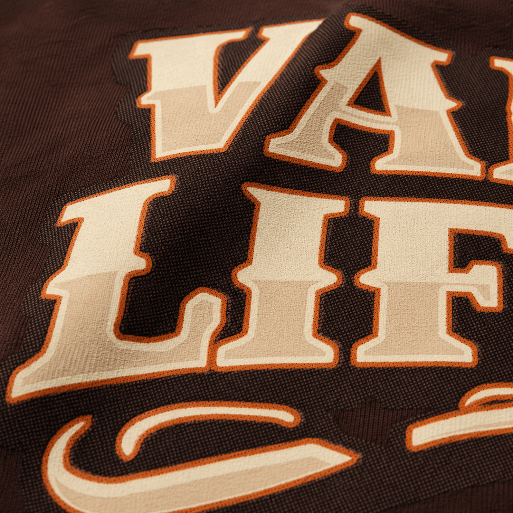 Close-up of a dark brown woven fabric with large cream lettering outlined in orange, showing part of the word 'VALLE' and 'LIFE'.