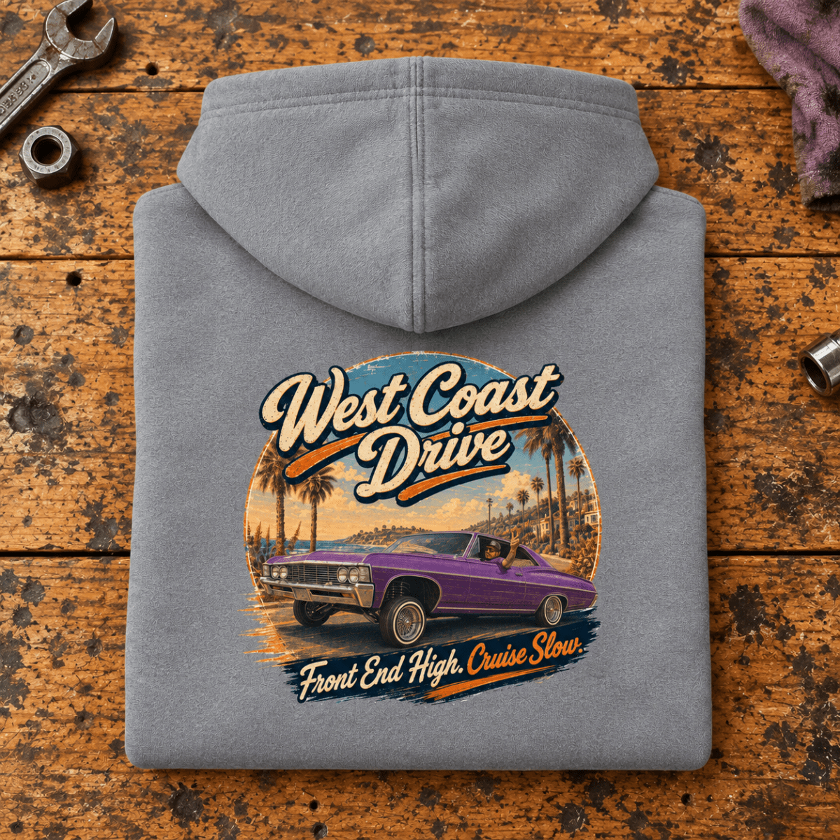 Lowrider Car Graphic Hoodie – West Coast Drive, folded back main hero on a worn automotive workbench – car-hd-0068